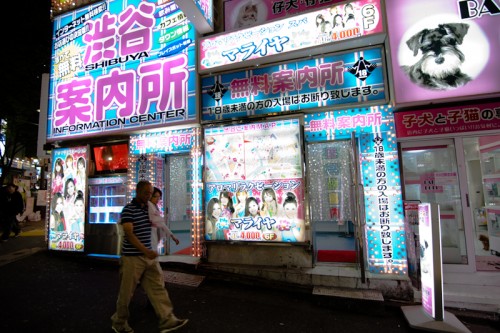 Two men walk past a "free information center" on Shibuya's Dogenzaka. The sign advertises aroma relaxation, ¥4,000 for 40 minutes.